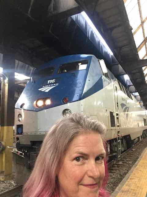 Selfie of a woman with pink and white hair in front of a train engine