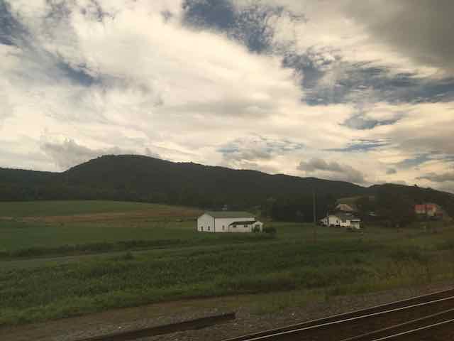 Rolling hills and farm buildings below big, luminous clouds