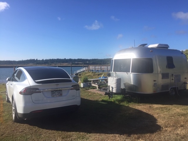 Car and camper next to a lake in bright sunlight.