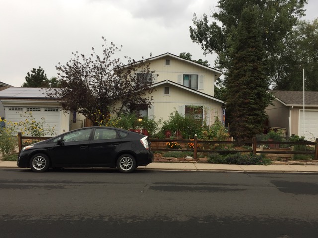 Car in front of a house with water-saving plants and solar panels on the garage.