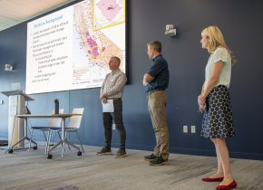 Three people stand in front of a projected slide with watershed maps to talk water data management.