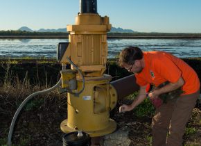 Person in an orange safety jacket samples a large well agricultural well.