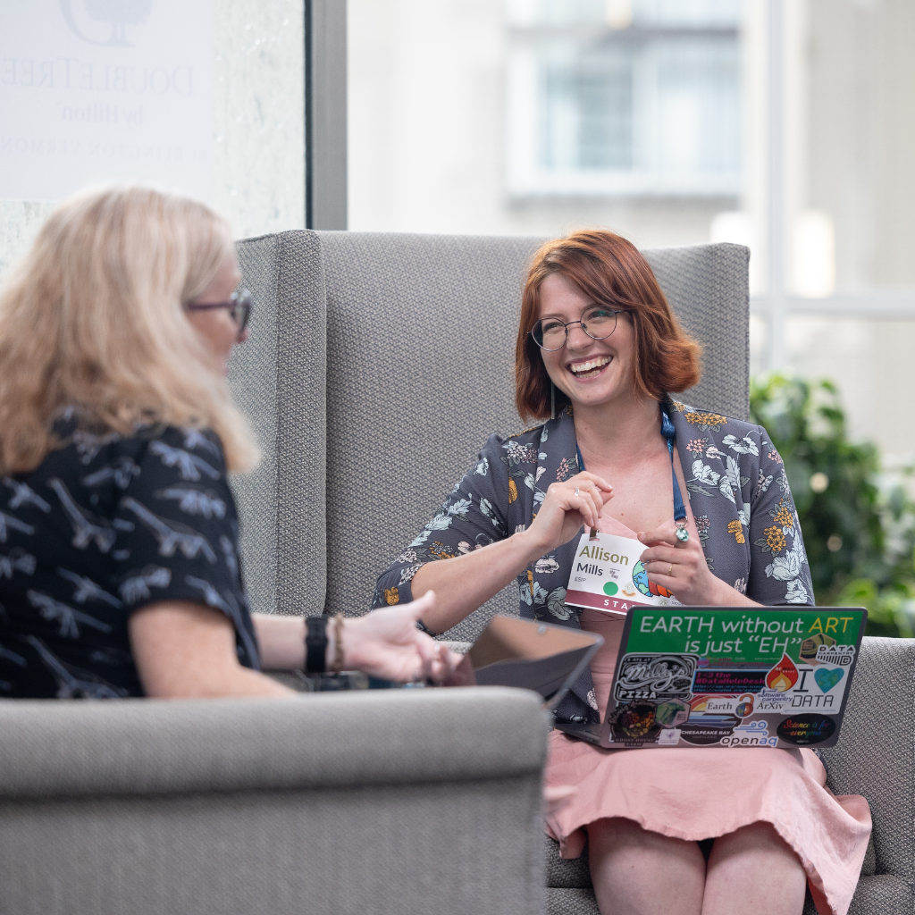 A person with a laptop covered in stickers smiles at another person.