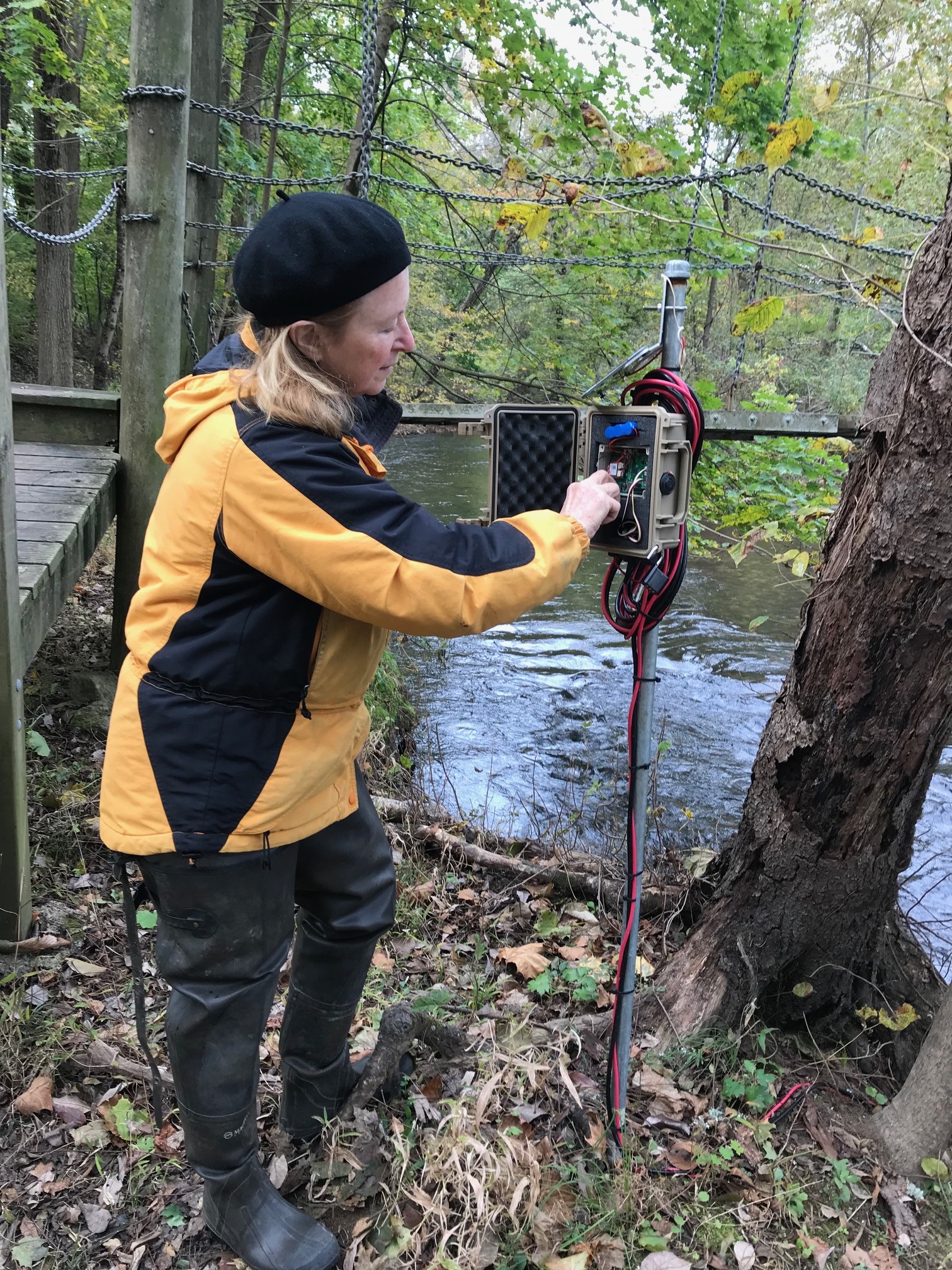 A citizen scientist interacting with water monitoring equipment on the bank of a river.