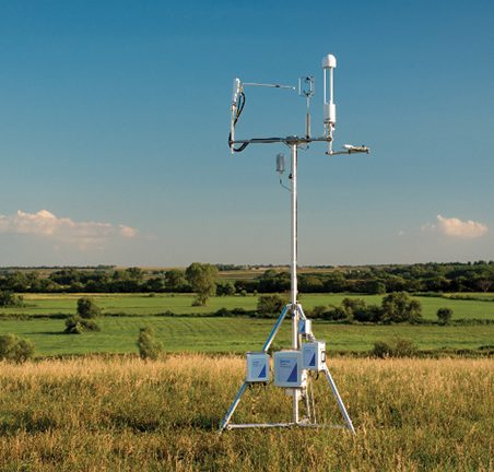 An eddy covariance tower in a sunlit grass field.